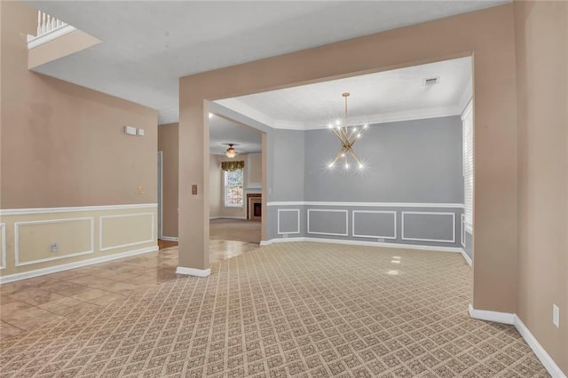 carpeted spare room with a notable chandelier, ornamental molding, a decorative wall, wainscoting, and a fireplace