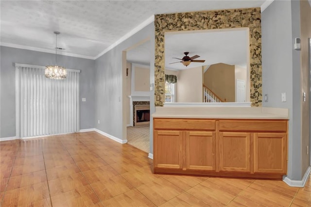 kitchen with ceiling fan with notable chandelier, decorative light fixtures, crown molding, a fireplace, and light countertops