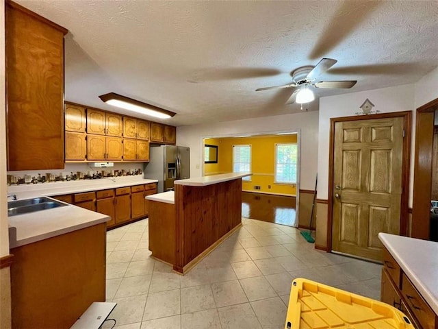 kitchen featuring a kitchen island, stainless steel fridge with ice dispenser, a textured ceiling, sink, and ceiling fan