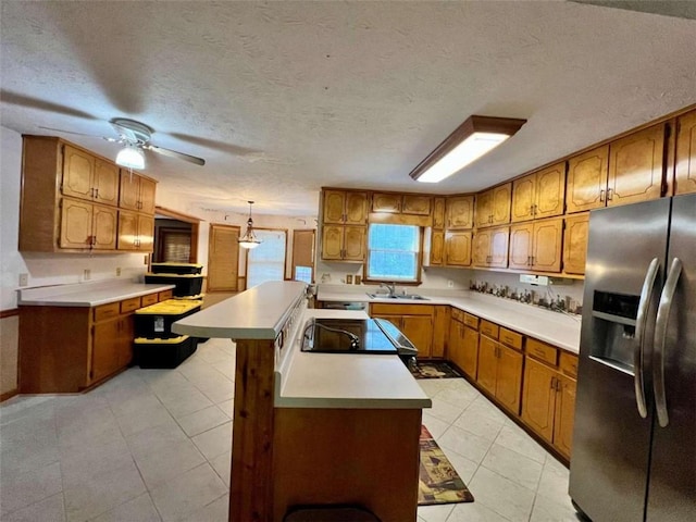 kitchen featuring a kitchen island, a textured ceiling, stainless steel refrigerator with ice dispenser, hanging light fixtures, and ceiling fan