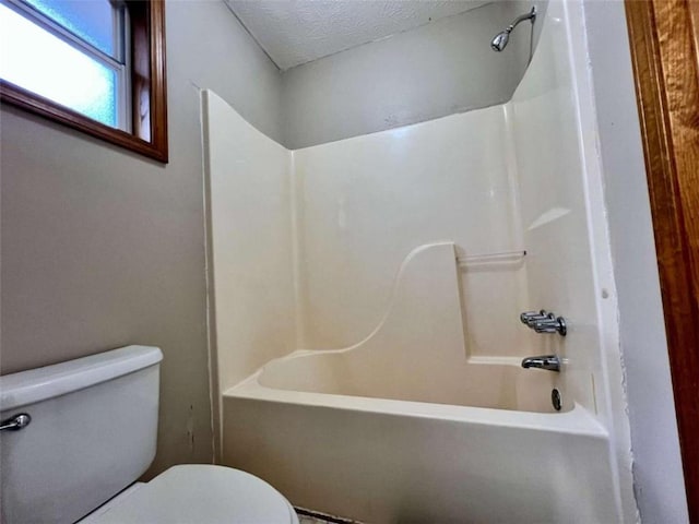 bathroom with a textured ceiling, toilet, and bathing tub / shower combination