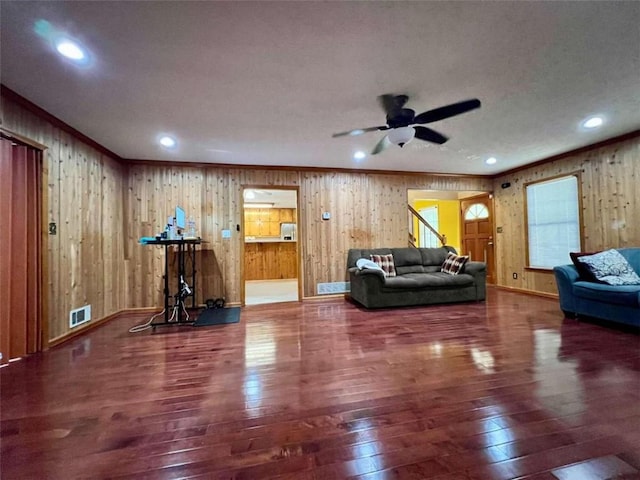 living room with dark wood-type flooring, wood walls, ornamental molding, and ceiling fan