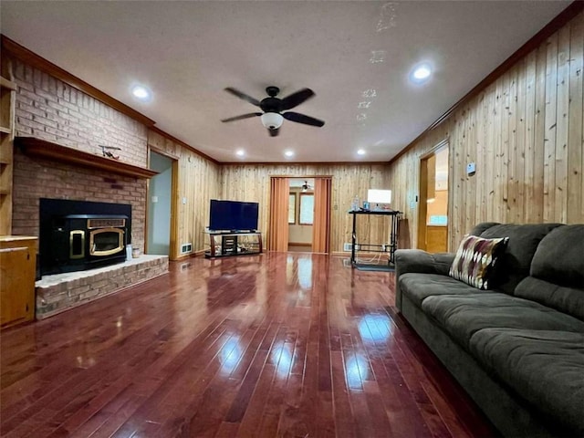 living room featuring wood walls, dark wood-type flooring, ceiling fan, and crown molding