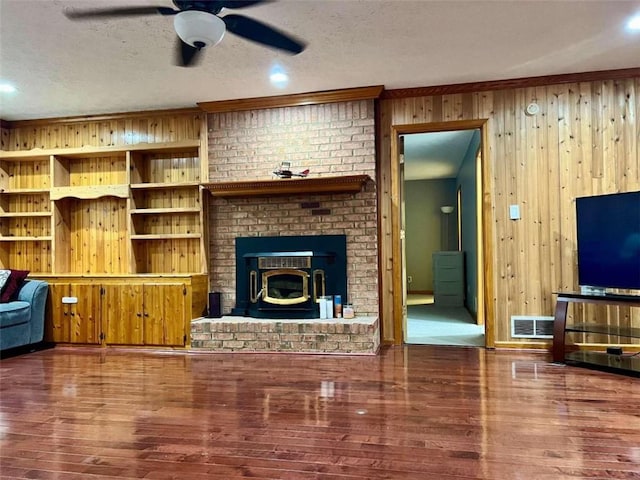 living room featuring ornamental molding, a textured ceiling, hardwood / wood-style floors, a wood stove, and wooden walls