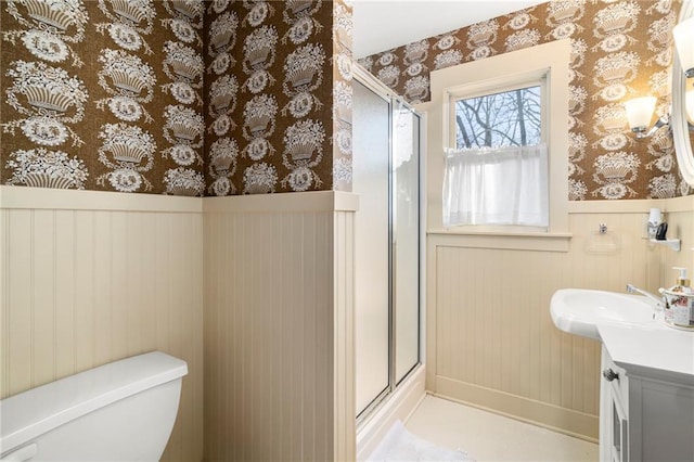 full bath featuring wallpapered walls, wainscoting, toilet, vanity, and a shower stall