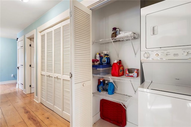 clothes washing area with light wood-type flooring, stacked washer and clothes dryer, baseboards, and laundry area