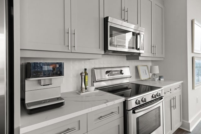 kitchen with light stone counters, gray cabinetry, stainless steel appliances, and baseboards