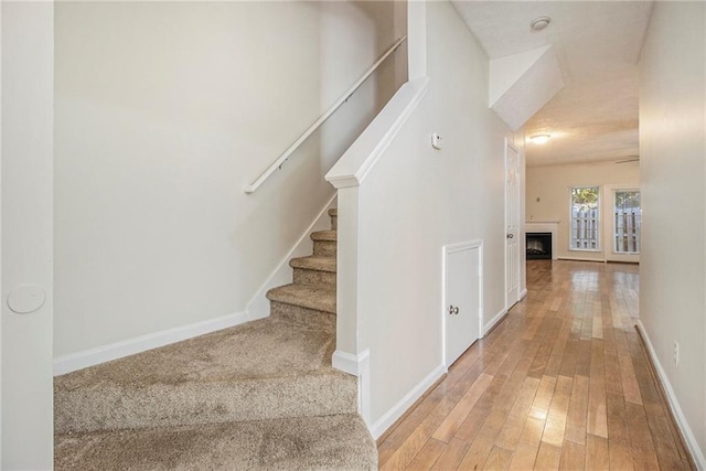 staircase with a fireplace, baseboards, and hardwood / wood-style floors