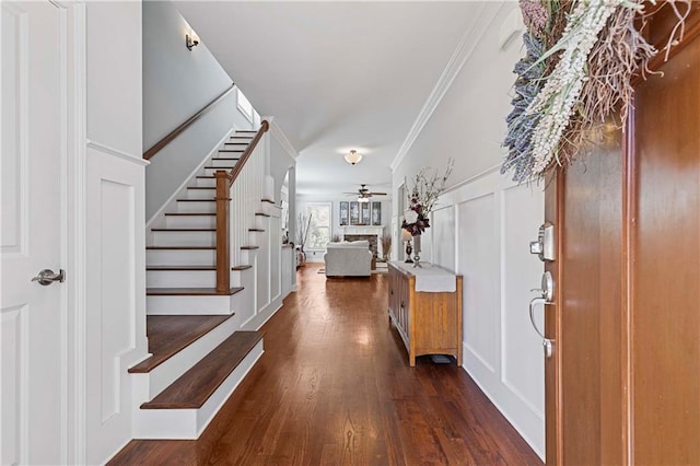 foyer with dark wood finished floors, a ceiling fan, ornamental molding, stairs, and a decorative wall