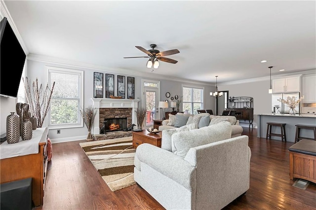 living room featuring plenty of natural light, ornamental molding, dark wood-type flooring, and a stone fireplace