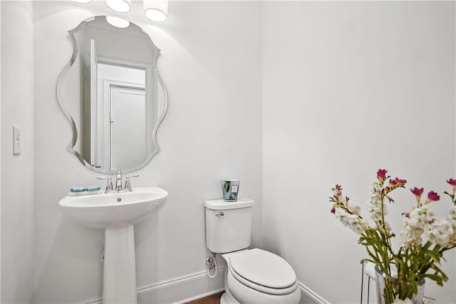 half bathroom featuring toilet, baseboards, and a sink