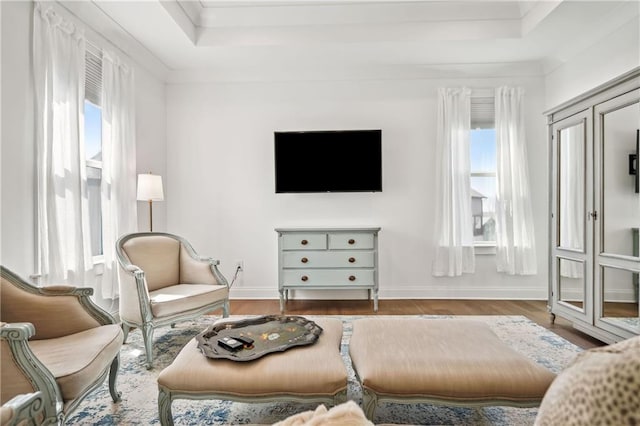 living area featuring a tray ceiling, baseboards, wood finished floors, and ornamental molding