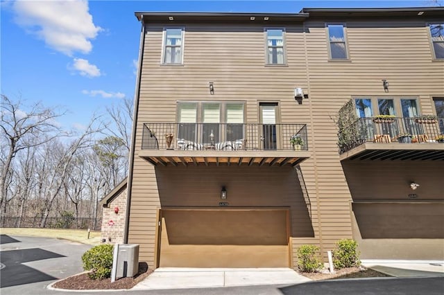 back of property featuring an attached garage, a balcony, and driveway