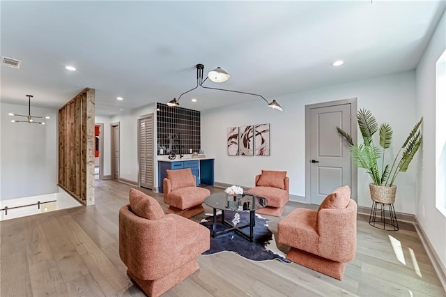 living room featuring bar area, a chandelier, and light wood-type flooring