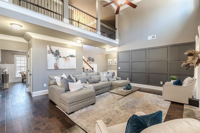 living room with ceiling fan, dark hardwood / wood-style flooring, ornamental molding, and a high ceiling