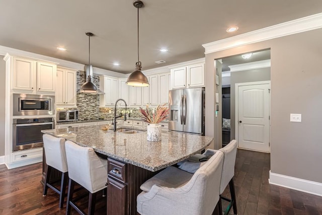 kitchen featuring appliances with stainless steel finishes, dark wood-type flooring, sink, a center island with sink, and hanging light fixtures