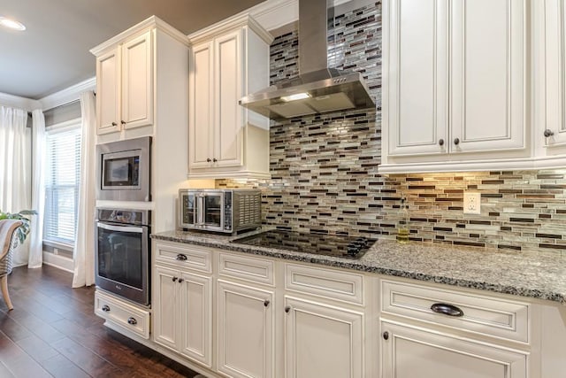 kitchen featuring backsplash, wall chimney exhaust hood, light stone counters, appliances with stainless steel finishes, and dark hardwood / wood-style flooring