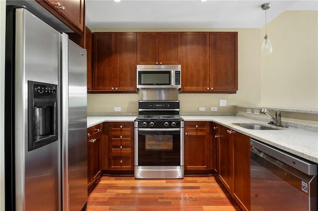 kitchen featuring appliances with stainless steel finishes, a sink, light wood finished floors, and decorative light fixtures