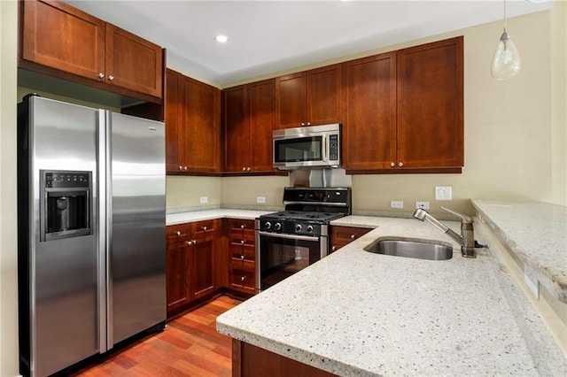 kitchen with stainless steel appliances, a sink, a peninsula, light wood-style floors, and light stone countertops
