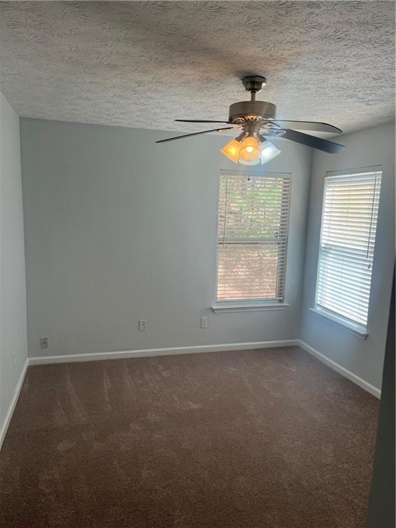 unfurnished room with baseboards, ceiling fan, dark carpet, and a textured ceiling