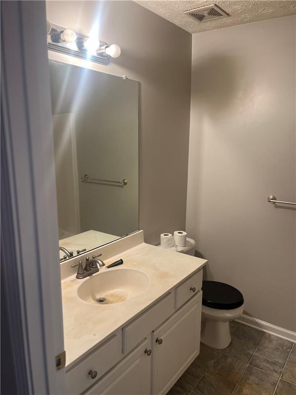 half bath with a textured ceiling, visible vents, toilet, tile patterned floors, and vanity