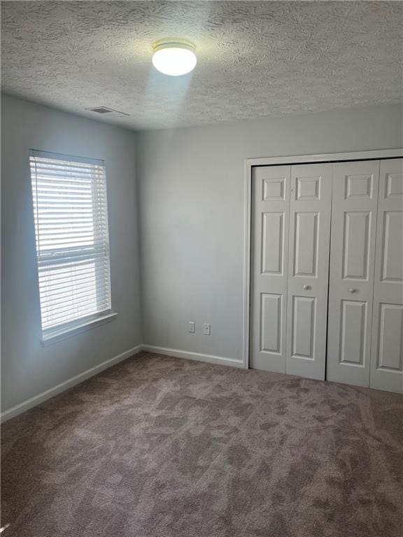 unfurnished bedroom featuring carpet flooring, baseboards, a textured ceiling, visible vents, and a closet