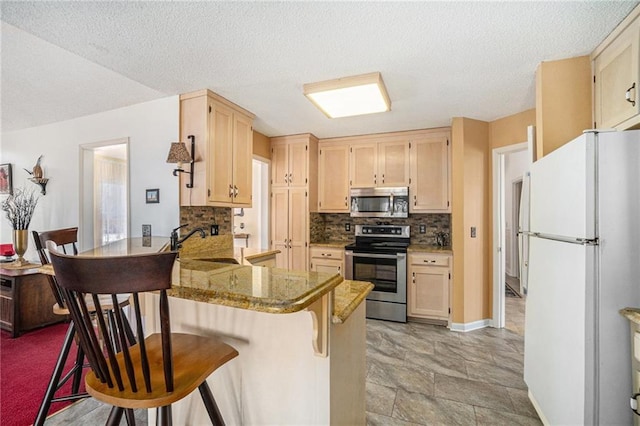 kitchen featuring a peninsula, a sink, light brown cabinetry, appliances with stainless steel finishes, and backsplash