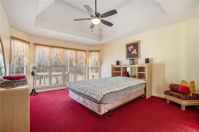 carpeted bedroom with ceiling fan, a tray ceiling, baseboards, and a textured ceiling