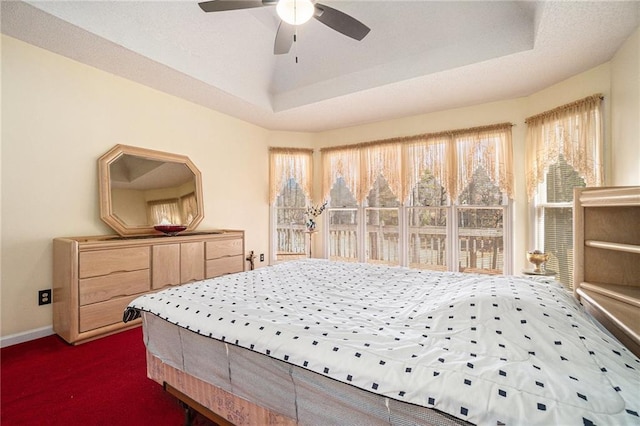 bedroom with ceiling fan, baseboards, a tray ceiling, and dark colored carpet