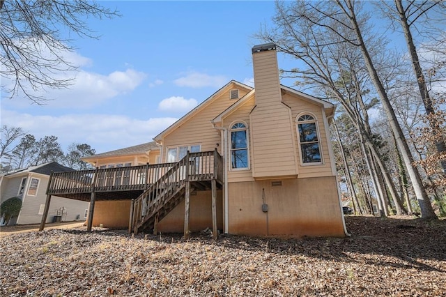 back of house featuring stairs, a chimney, and a wooden deck