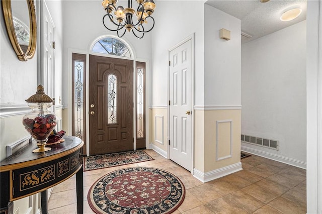 tiled entrance foyer with visible vents, baseboards, and an inviting chandelier