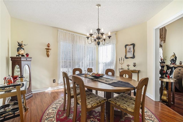 dining space with baseboards, a textured ceiling, an inviting chandelier, and wood finished floors