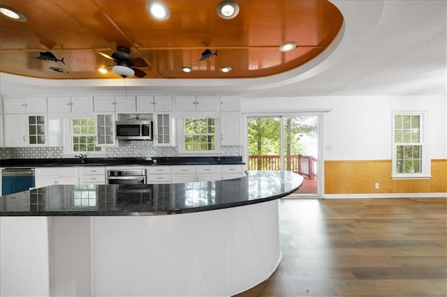 kitchen with appliances with stainless steel finishes, wood-type flooring, white cabinetry, and a tray ceiling