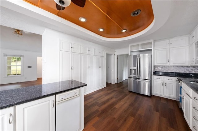 kitchen with white cabinetry, appliances with stainless steel finishes, dark hardwood / wood-style floors, a tray ceiling, and dark stone counters