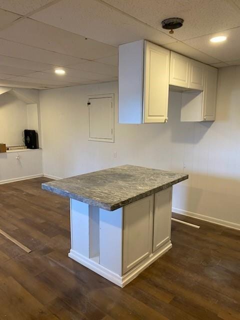 kitchen featuring dark wood-type flooring, dark stone countertops, a drop ceiling, and white cabinets