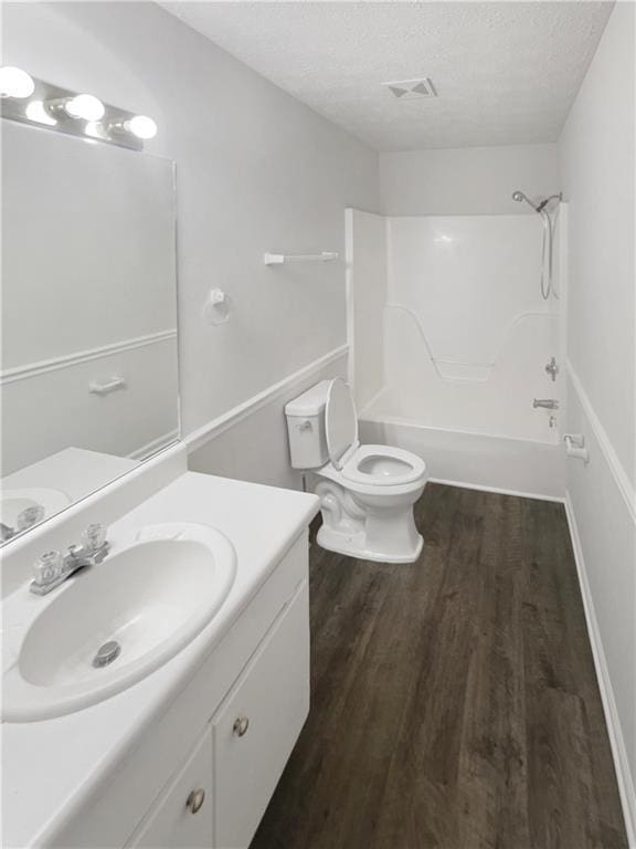 full bathroom with wood-type flooring, vanity,  shower combination, toilet, and a textured ceiling