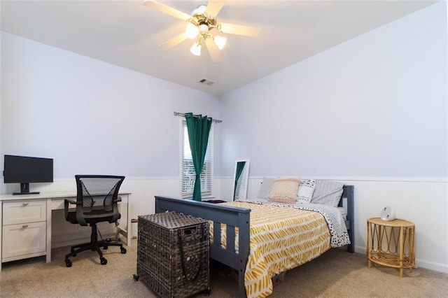 bedroom featuring light carpet, a wainscoted wall, visible vents, and a ceiling fan