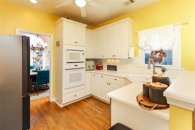 kitchen featuring white appliances, wood finished floors, a sink, visible vents, and white cabinets