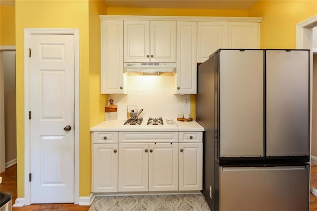 kitchen with under cabinet range hood, white gas cooktop, white cabinetry, light countertops, and freestanding refrigerator