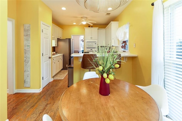 kitchen with a peninsula, a ceiling fan, white cabinets, light wood-style floors, and freestanding refrigerator