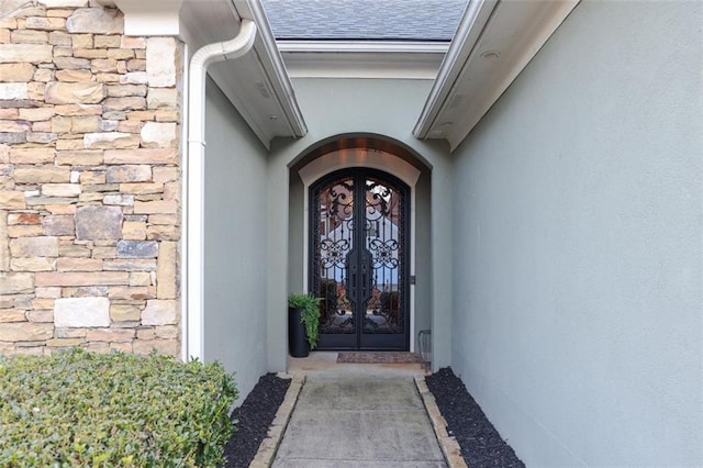 doorway to property featuring stone siding, stucco siding, french doors, and roof with shingles