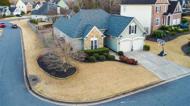 view of front of home featuring a garage, a shingled roof, stone siding, concrete driveway, and a residential view