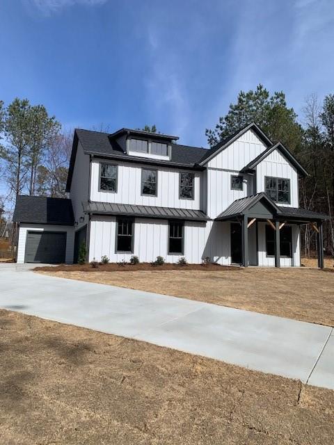 modern farmhouse featuring an attached garage, board and batten siding, a standing seam roof, metal roof, and driveway