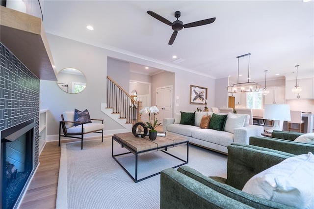 living area with a fireplace, crown molding, light wood-style flooring, baseboards, and stairs