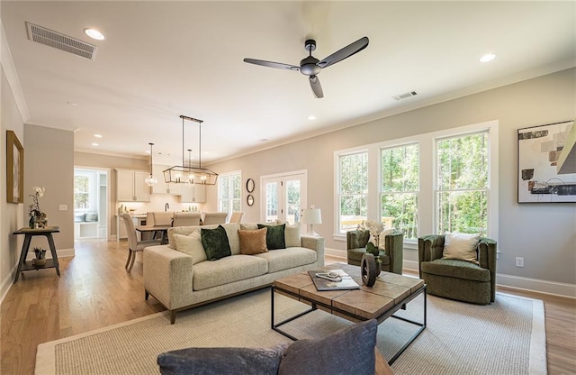 living area with ornamental molding, light wood-style flooring, and visible vents