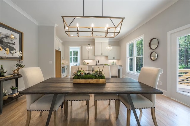 dining area with light wood-style flooring, ornamental molding, a chandelier, and baseboards