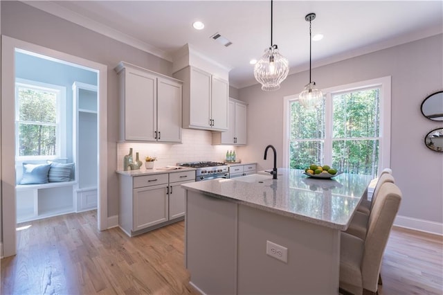 kitchen with white cabinets, hanging light fixtures, light stone countertops, a kitchen island with sink, and high end stove