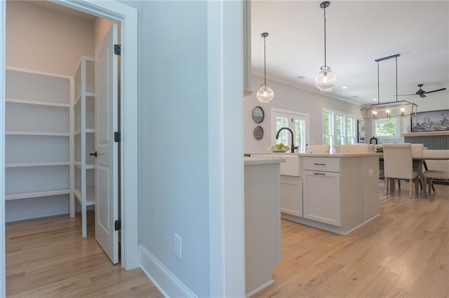 kitchen featuring white cabinets, light countertops, crown molding, light wood-style floors, and pendant lighting