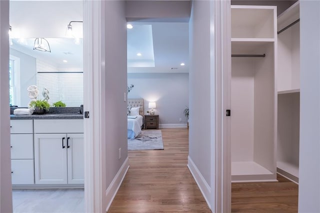 corridor with light wood-style floors, recessed lighting, a sink, and baseboards