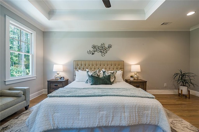 bedroom with a raised ceiling, visible vents, and wood finished floors